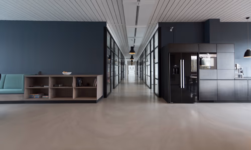 A wide open-plan corporate office with empty modern workstations, ergonomic chairs, and large windows letting in afternoon light — representing the changing landscape of tech employment as Microsoft offers voluntary retirement buyouts to 8,750 experienced US workers while simultaneously reporting record-breaking AI-driven revenue growth.