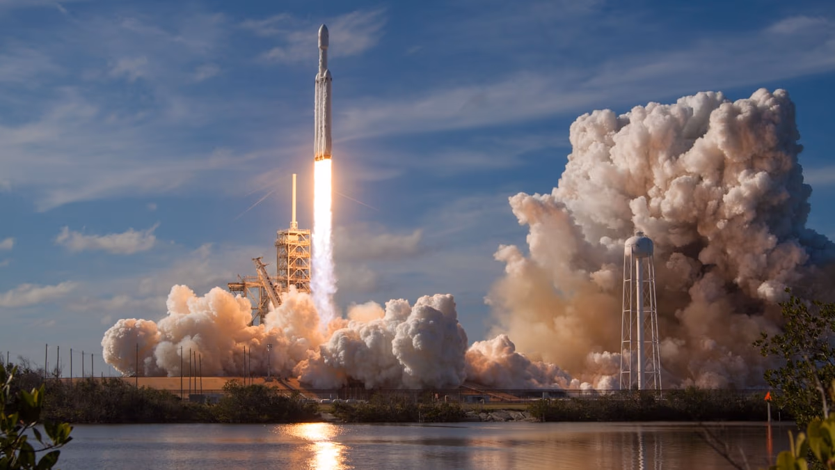 A SpaceX Falcon 9 rocket launching at night against a deep blue sky with a brilliant white exhaust plume — representing Elon Musk's ambition to take SpaceX into AI coding infrastructure through its $60 billion deal with Cursor, the leading AI code editor used by over half the Fortune 500.